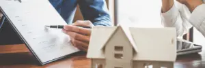 photo of a wood house on a table with two people talking about a home contract